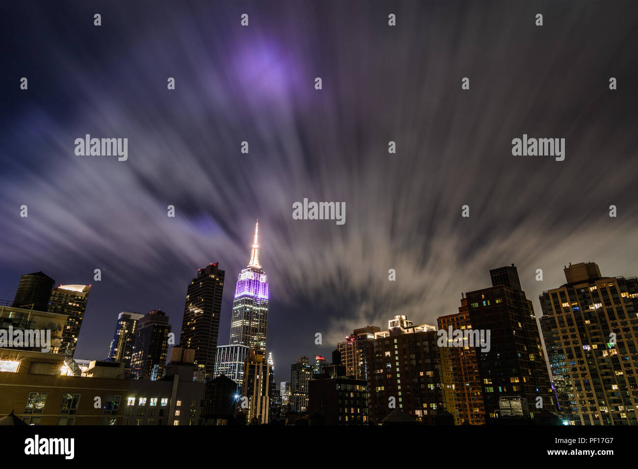 L'Empire State Building illuminato di notte come in movimento rapido flusso di nuvole sopra il quartiere di Chelsea di New York City. Foto Stock