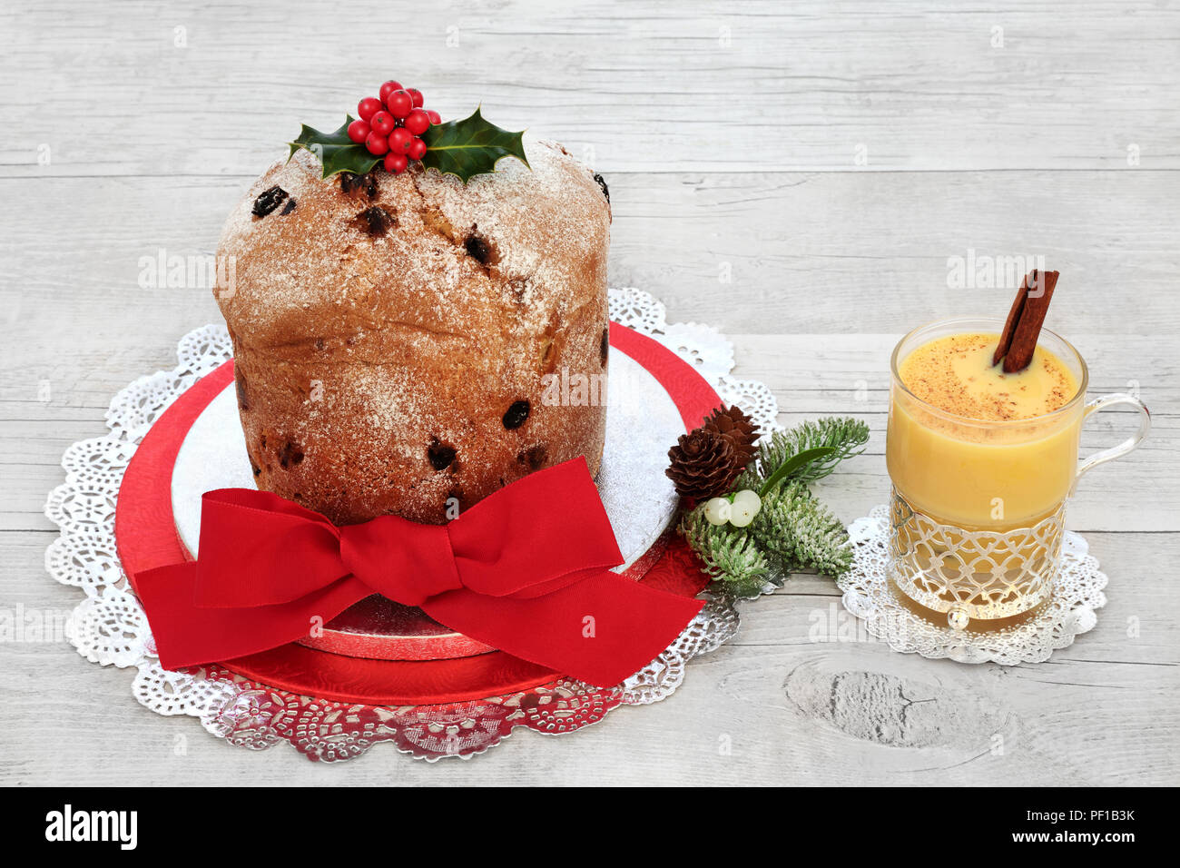 Il Panettone dolce di Natale di vetro e di zabaione con flora invernale di holly, abete e vischio su legno rustico sfondo. Dolce tradizionale pane. Foto Stock