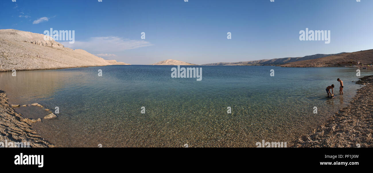 Croazia, Europa: i bagnanti a Rucica, la spiaggia di ciottoli si trova in una sterile baia circondata da un paesaggio desertico sulla famosa isola di Pag Foto Stock