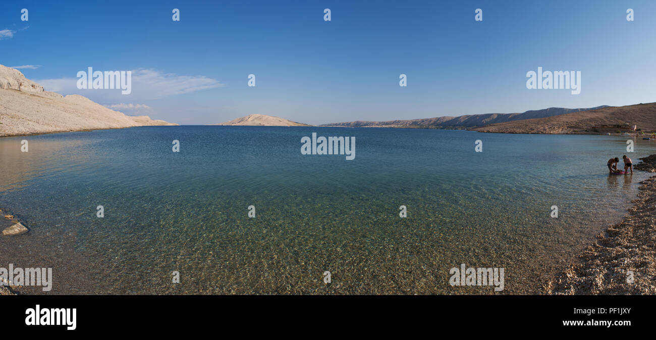 Croazia, Europa: i bagnanti a Rucica, la spiaggia di ciottoli si trova in una sterile baia circondata da un paesaggio desertico sulla famosa isola di Pag Foto Stock