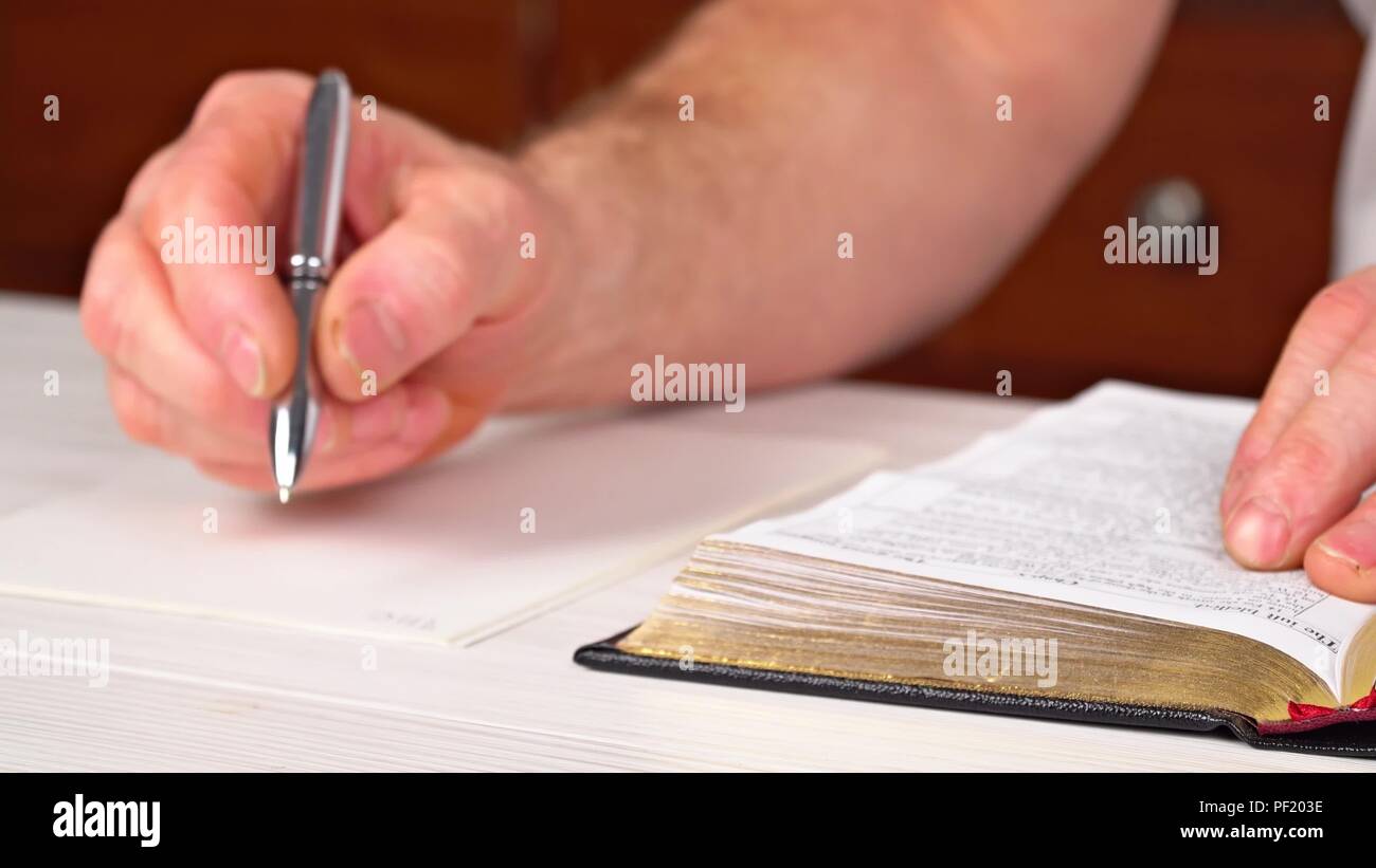 L uomo è in possesso di una penna in mano con un libro aperto che giace in fornt di lui le letture della domenica, la Bibbia Foto Stock