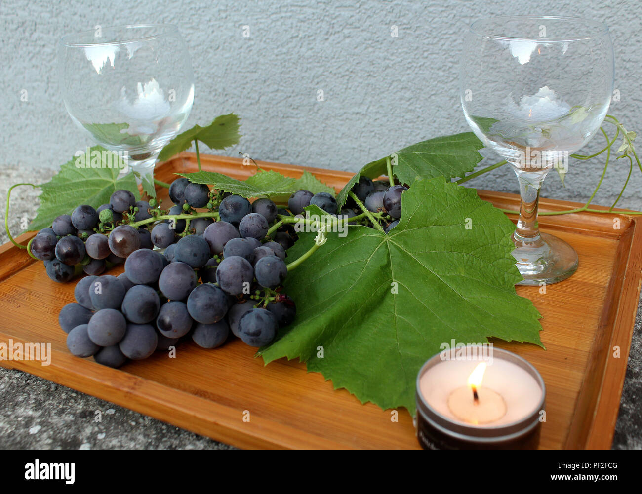 Still Life - svuota il bicchiere da vino, uve blu e foglie disposte su un vassoio in legno Foto Stock