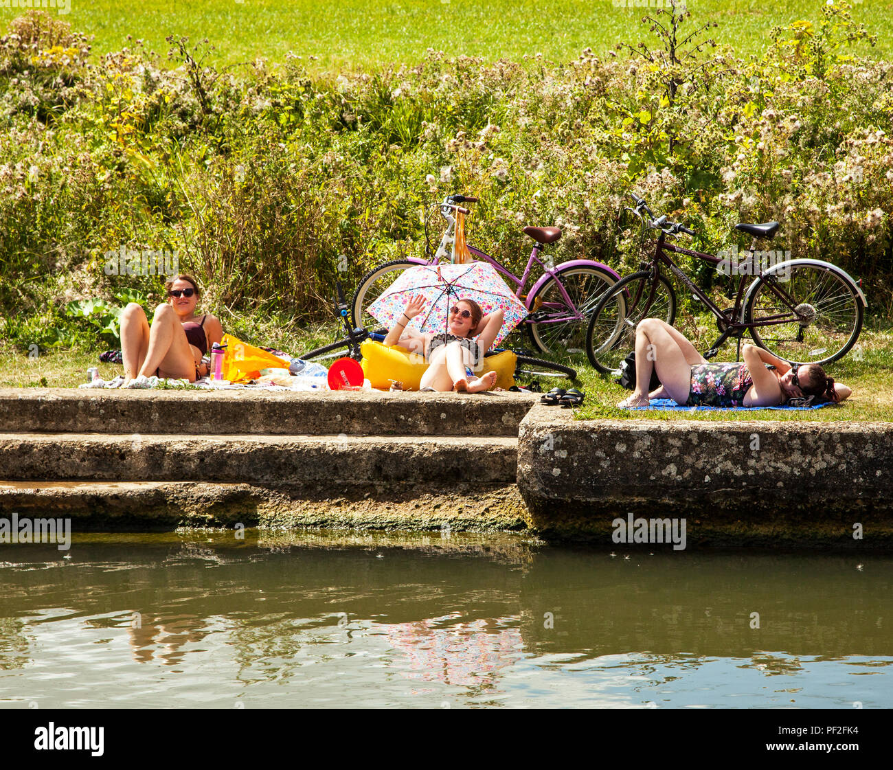 Ragazze donne e giovani donne con le loro biciclette cicli a prendere il sole sulle rive del fiume Tamigi sotto un ombrellone ombrellone durante la canicola del 2018 Foto Stock
