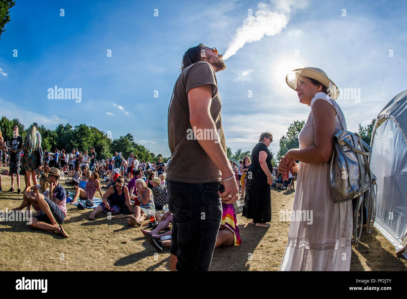 Un uomo vaping parla di una donna in un ampia colmato hat a un open air festival di musica su una calda giornata a Londra Foto Stock