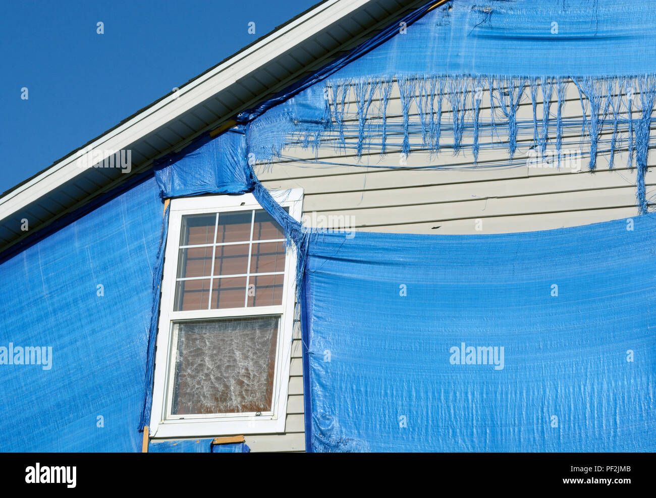Dettaglio della tempesta di grandine danneggiato home protetto da blue tarp weathered e triturato dalle tempeste successiva, il sole e il vento Foto Stock