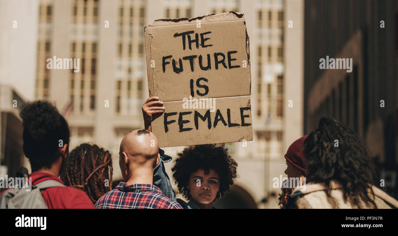Donna di marzo segno di protesta che legge il futuro è femmina. Femmina di camminare sulla via della città tenendo un banner con un gruppo di persone. Foto Stock