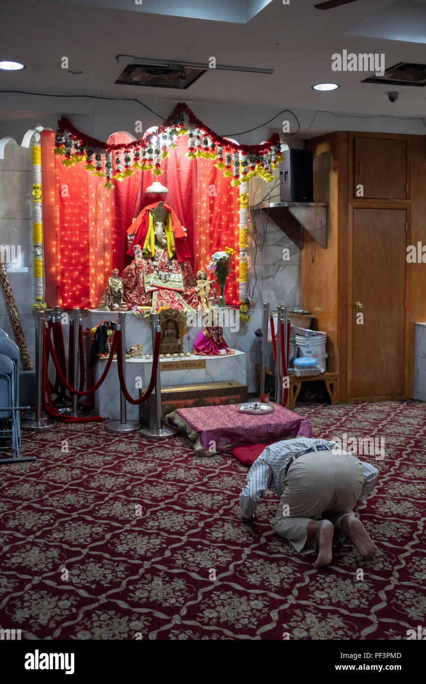 Un uomo di mezza età si inginocchia davanti alla statua di Ganesh a Satya Narayan Mandir in Elmhurst, Queens, a New York Foto Stock