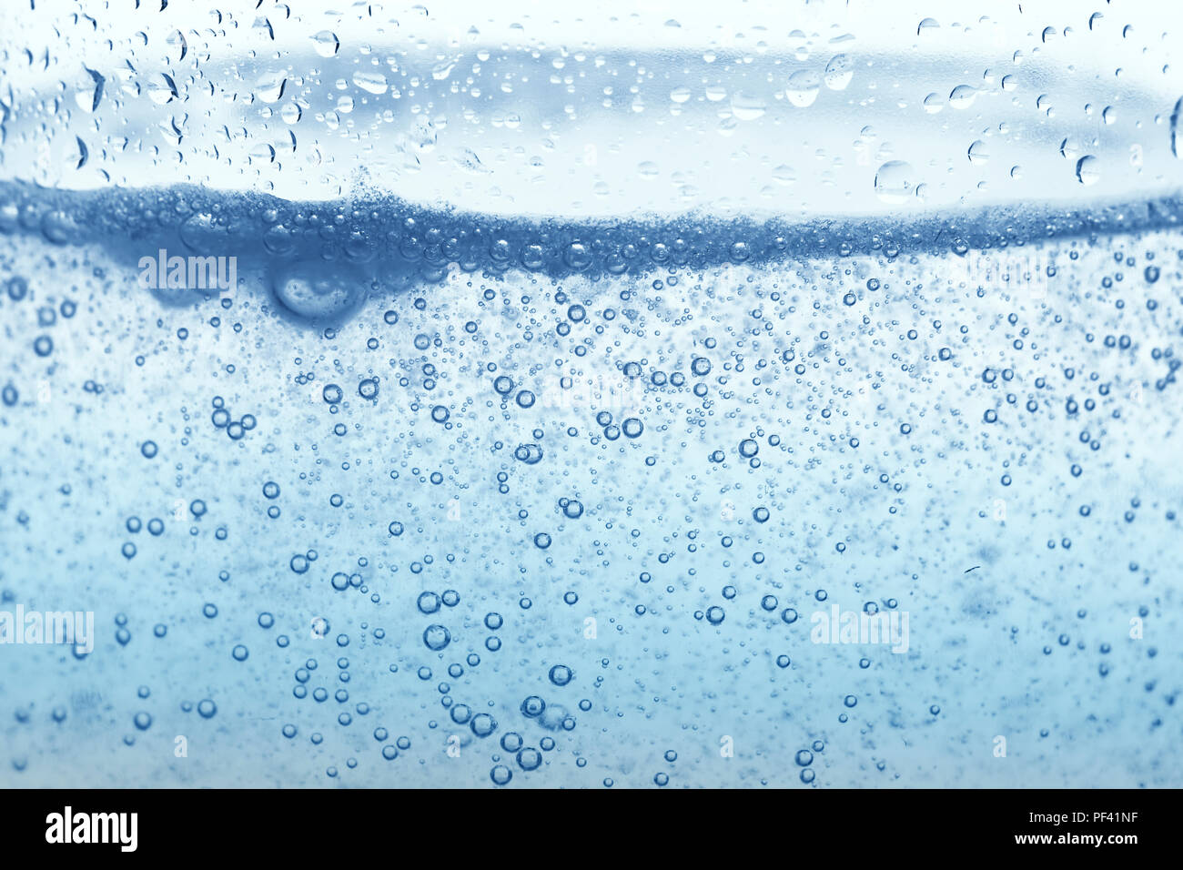Bolle di ossigeno in un bicchiere di acqua su uno sfondo blu. Acqua minerale. Sfondo. Macro.Texture. Foto Stock