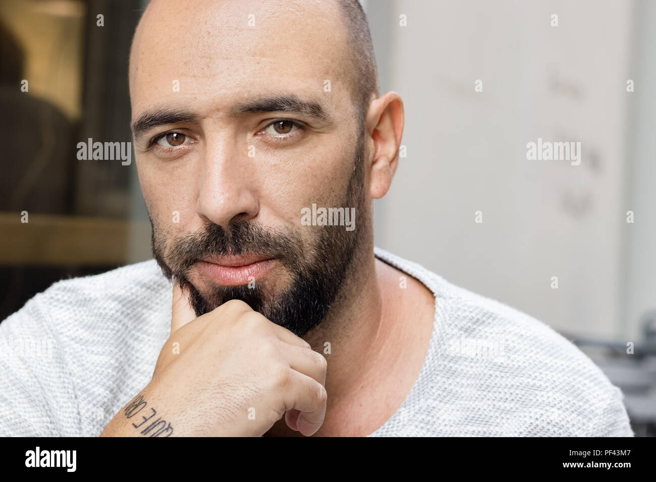 Ritratto di un uomo spagnolo con la barba guardando la telecamera, serio e pensieroso con una mano sul suo mento. Foto Stock