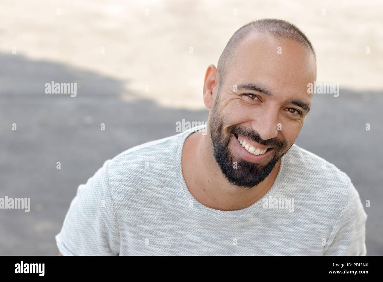 Ritratto di un uomo spagnolo con la barba a sorridere guardando la telecamera, indossando un cappello snapback e una t-shirt, all'esterno. Foto Stock