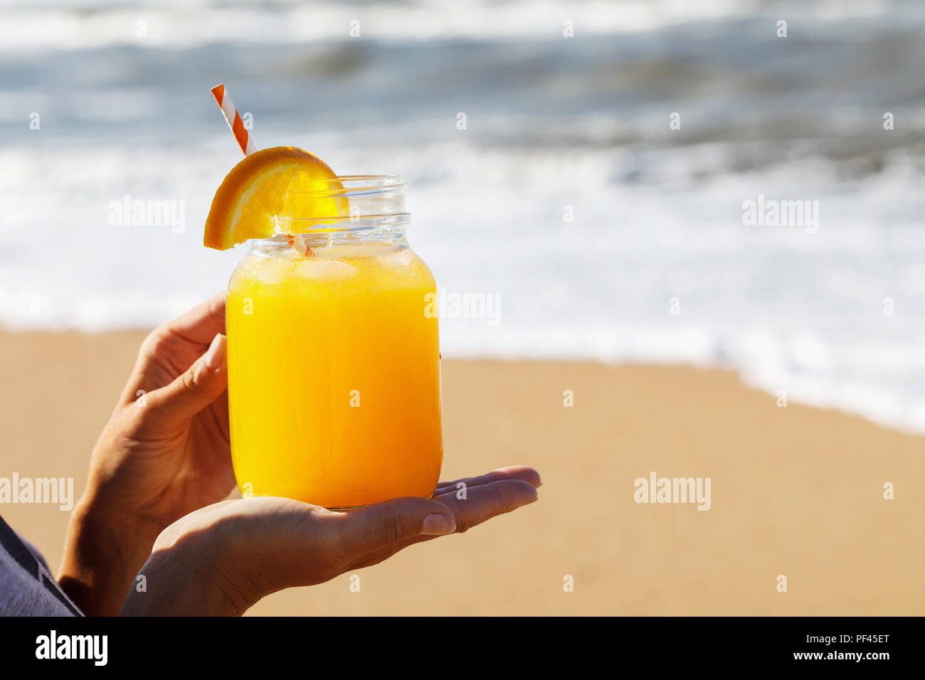 Succo di arancia con polpa in mani sulla spiaggia con spazio per il testo Foto Stock