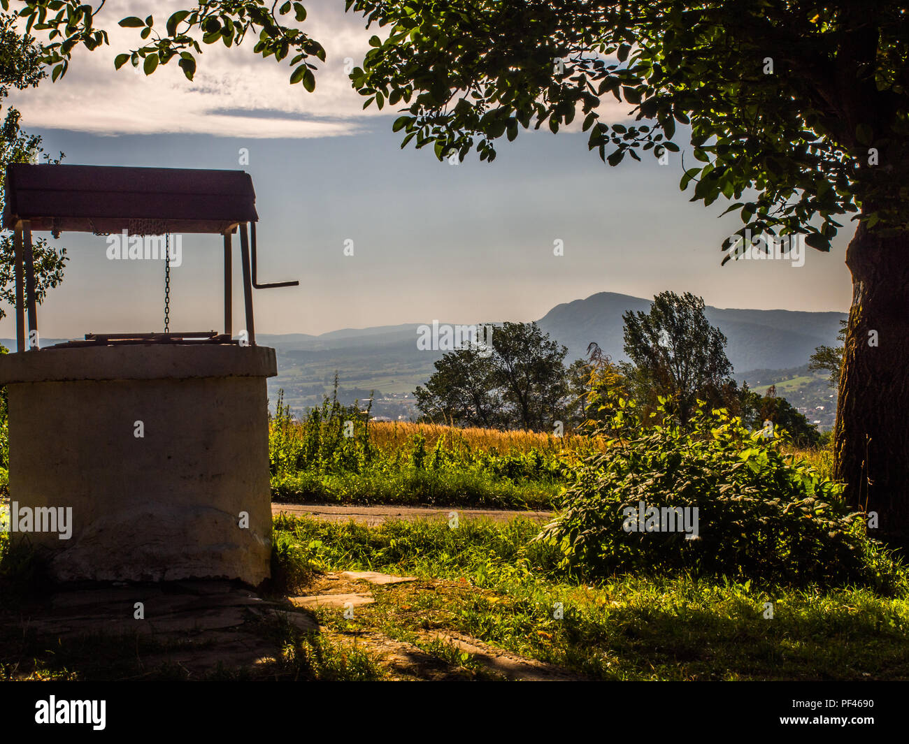 Vecchio, pietra, acqua bene con un verricello a manovella e nel villaggio polacco e la vista delle Cergowa Hill in bassa Beskids, Beskid Niski, Polonia Foto Stock