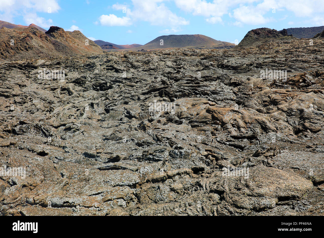 Flusso di lava solidificato e crosta con montagne vulcaniche sullo sfondo nel Parco Nazionale di Timanfaya, Lanzarote, Isole Canarie Foto Stock