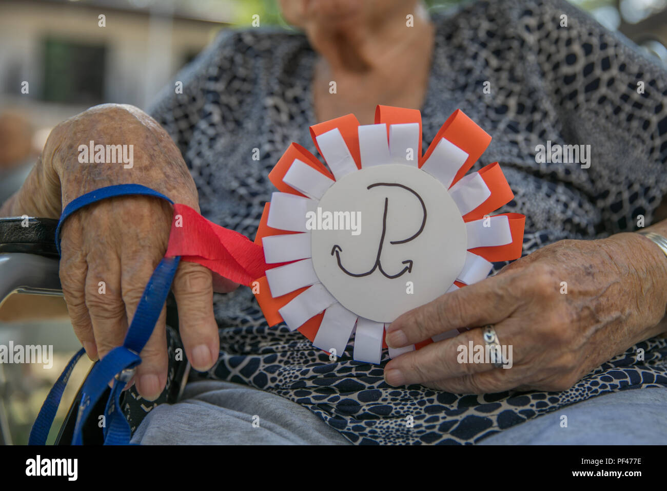 Le mani della donna anziana con il bianco e il rosso cotillion con sovrapposte emblema di ancoraggio della resistenza polacca. Anniversario dell'Insurrezione di Varsavia. Il polacco sy Foto Stock