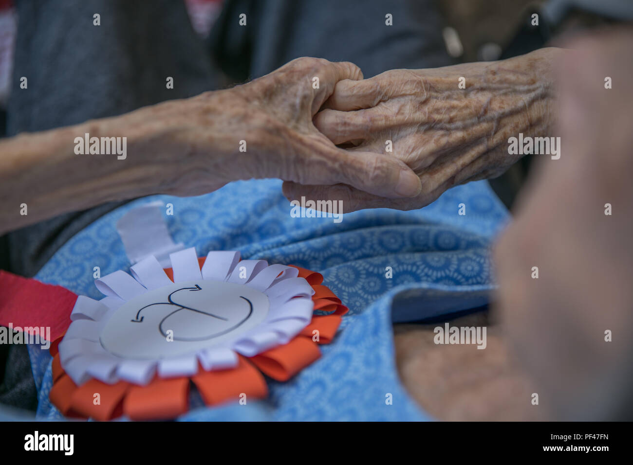 Le mani della donna anziana con il bianco e il rosso cotillion con sovrapposte emblema di ancoraggio della resistenza polacca. Anniversario dell'Insurrezione di Varsavia. Il polacco sy Foto Stock