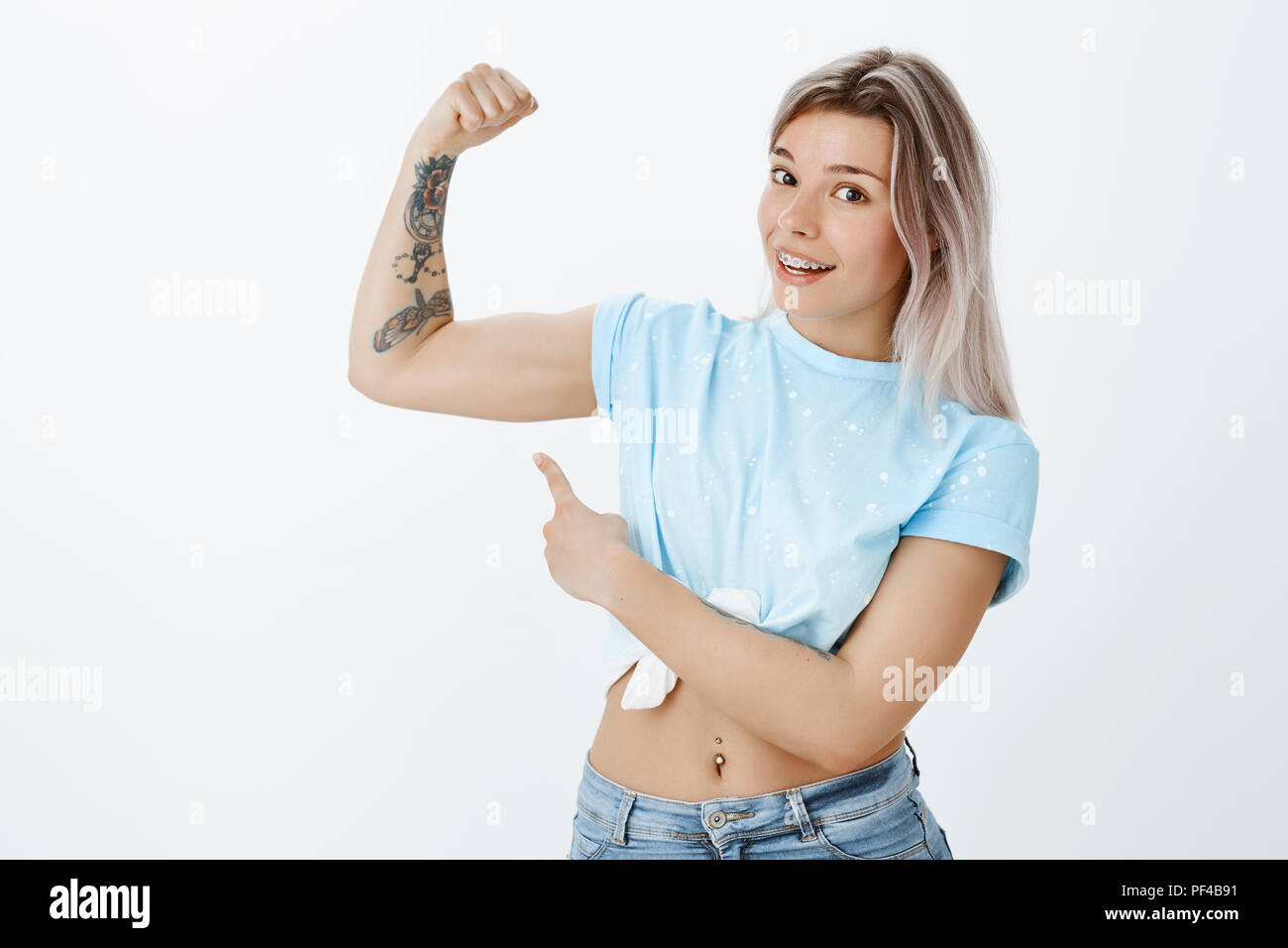 Certo si può battere me, guardare questo muscolo. Positivo gioiosa donna attraente con grande corpo, sollevamento braccio tatuato e puntando al bicipite con il dito indice, lavorando fuori e conduce uno stile di vita sano Foto Stock