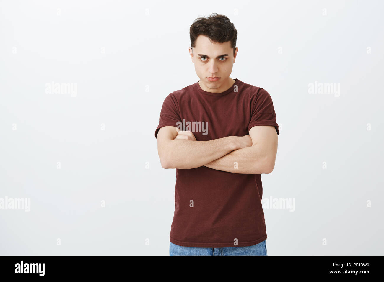 Offeso deluso ragazzo attraente in abiti casual, tenendo le mani incrociate sul petto e guardando da sotto la fronte con visto di buon occhio le sopracciglia e male grimace aggressivo, esprimendo l'odio e il disprezzo Foto Stock