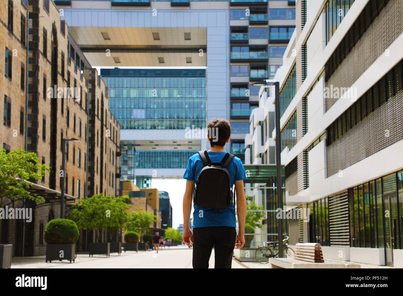 Vista posteriore di un giovane uomo con zaino appena arrivati in città grande e cercando di edifici moderni con prospettive ed opportunità, Cologne City dist Foto Stock