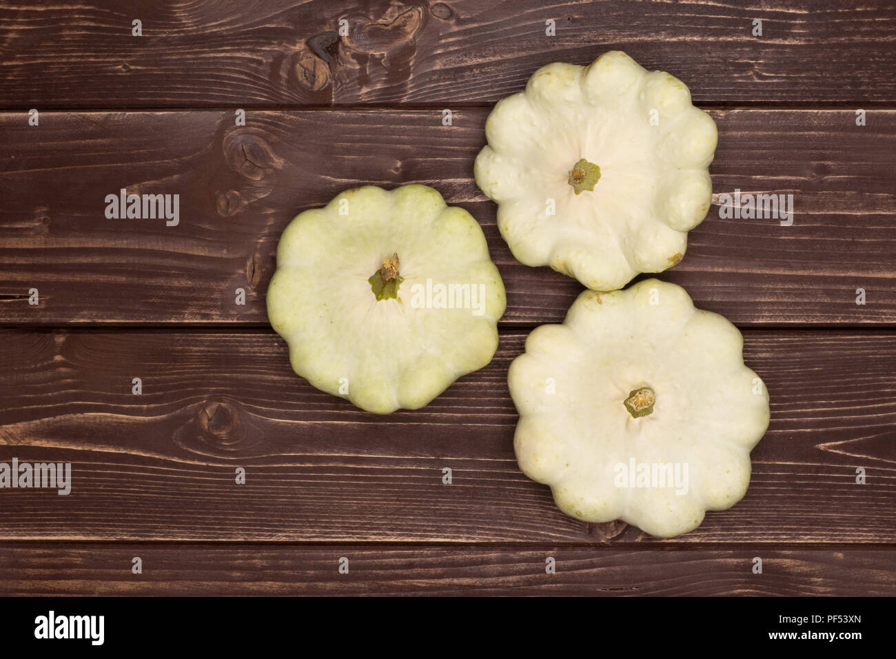 Gruppo di tre intera estate white pattypan squash flatlay su legno marrone Foto Stock