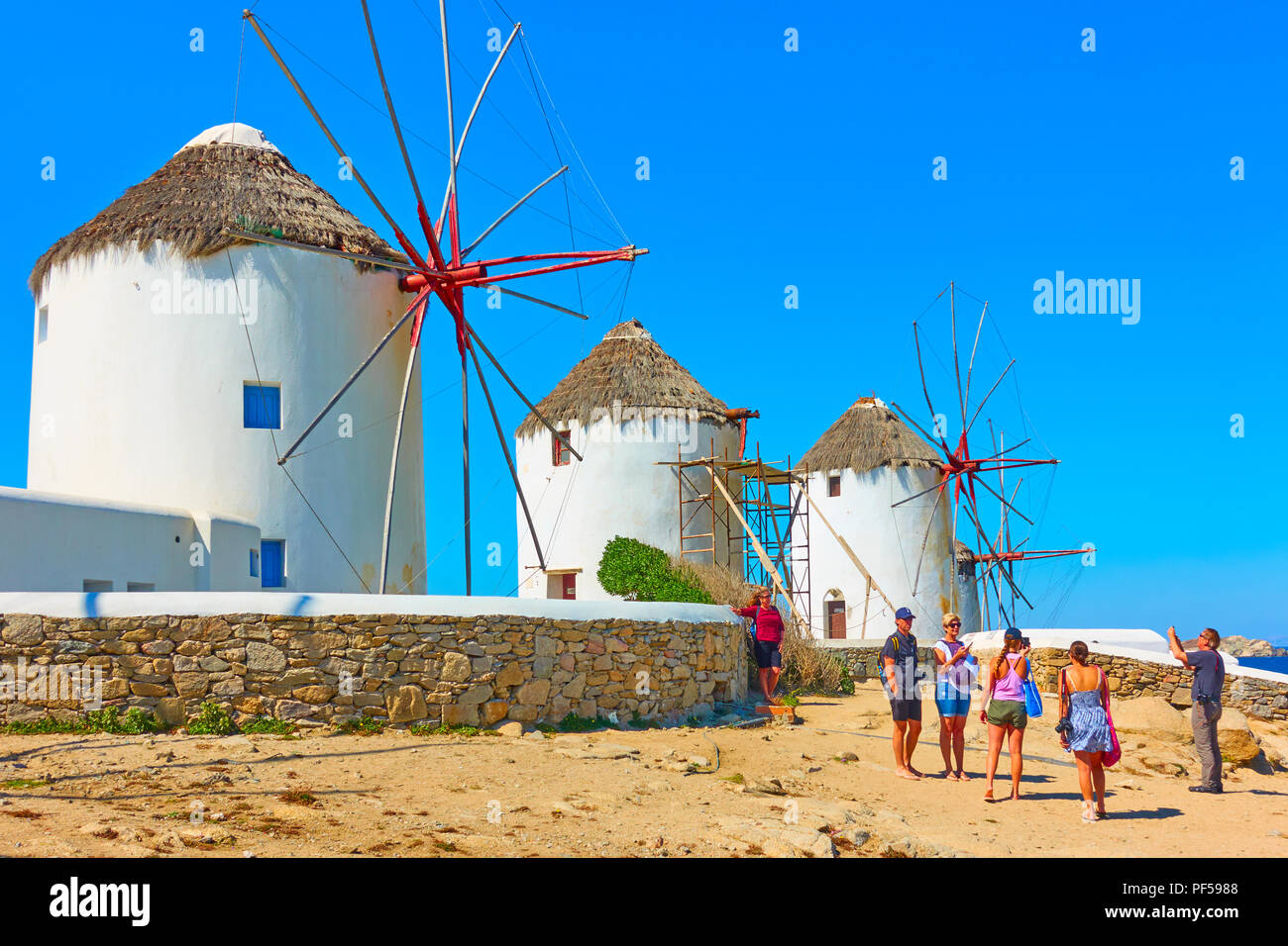 Mykonos, Grecia - 22 Aprile 2018: turisti scattare foto accanto ad antichi mulini a vento sulla riva del mare nell'isola di Mykonos Foto Stock