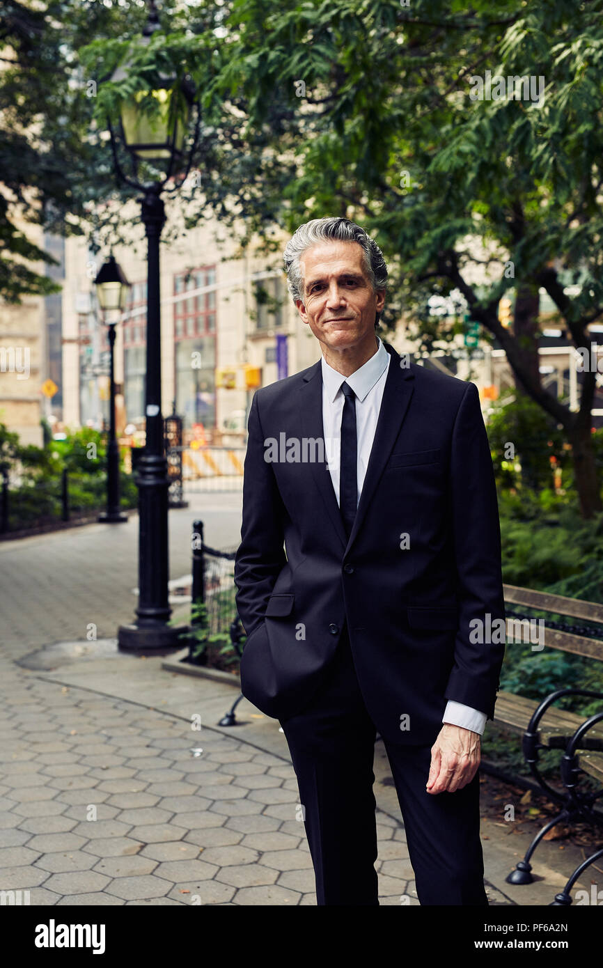 Capelli grigi Man in Black Suit le passeggiate attraverso un parco Foto Stock