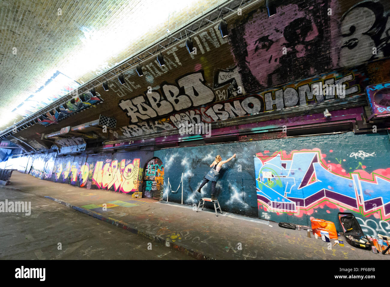 Un artista la spruzzatura di vernice sul muro in un tunnel in London, London, England, Regno Unito Foto Stock
