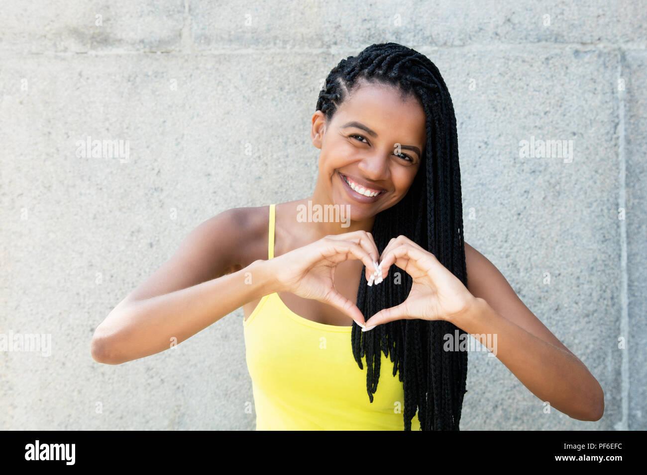African American donna con dreadlocks in amore che mostra il cuore con le mani all'aperto in estate Foto Stock