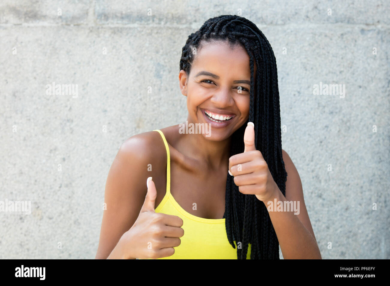 Felice di ridere americano africano donna con dreadlocks che mostra i pollici all'aperto in estate Foto Stock