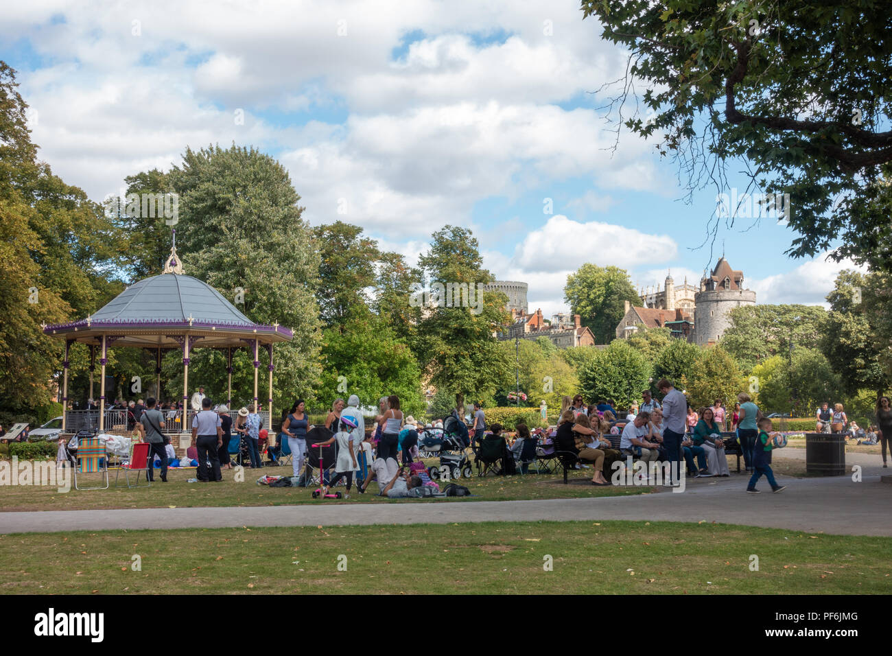 Una band suona un concerto gratuito nella band stand in giardini Alexandra in Windsor, Regno Unito. Persone sedersi su sedie pieghevoli, benchses e il pavimento a guardare. Foto Stock