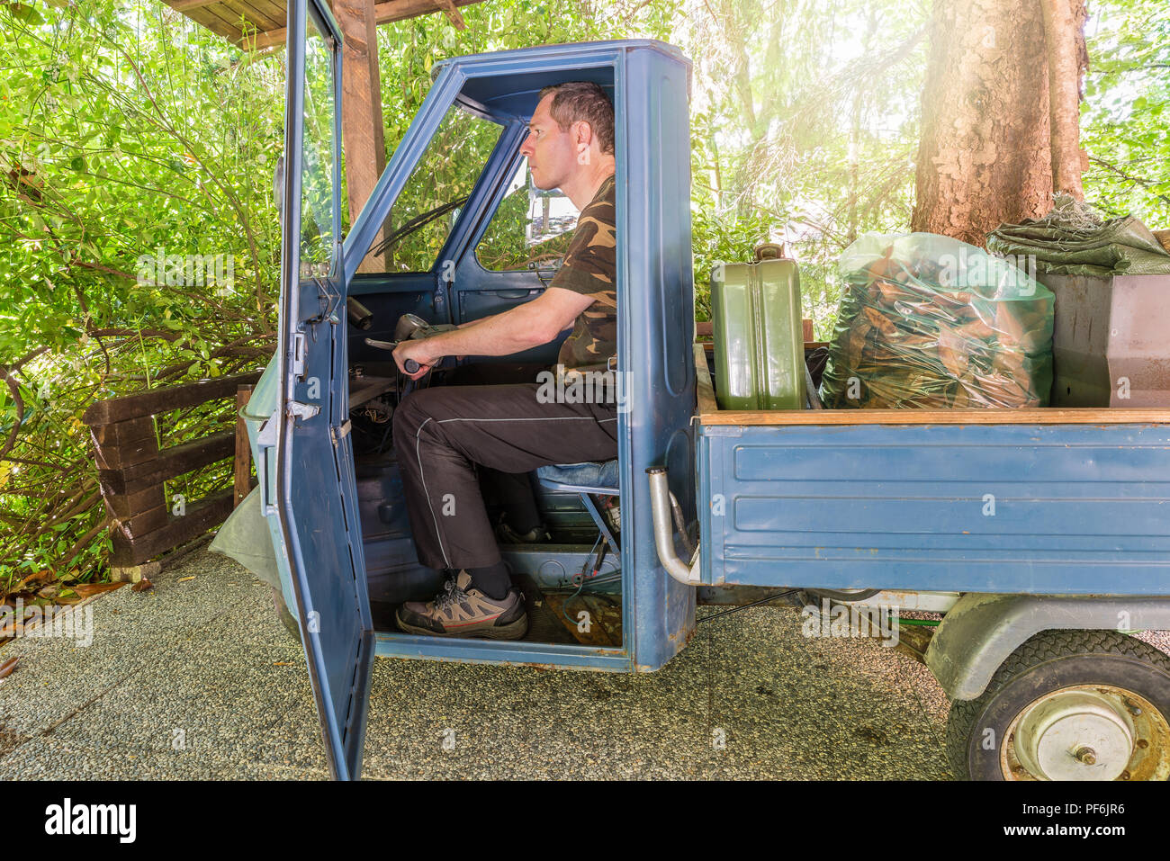 Uomo in una vecchia tre ruote monoposto di veicolo, modello prodotto tra 1984 e 1985 utilizzato per il giardinaggio Foto Stock