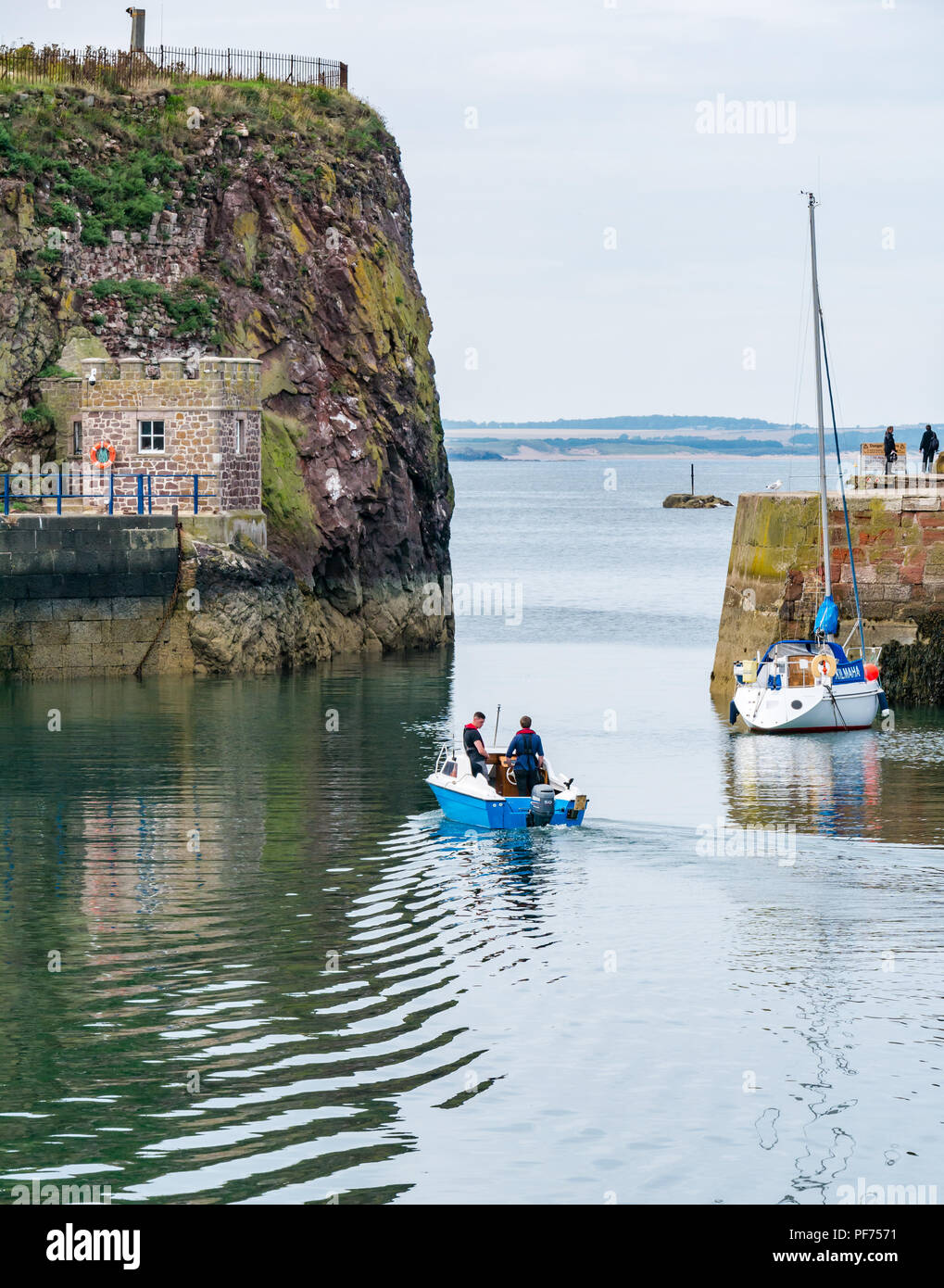 Dunbar, East Lothian, Scozia, Regno Unito, 20 agosto 2018. UK Sunshine in Dunbar harbor. Due uomini di lasciare il porto in una piccola barca con un yacht ormeggiati Foto Stock