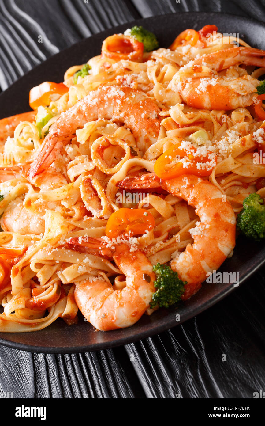 Ricetta italiana pasta fettuccine con gamberi, calamari, broccoli, formaggio con salsa di pomodoro closeup su di una piastra verticale. Foto Stock