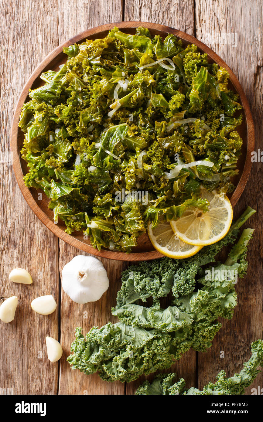 Foglie di cavolo stufato con cipolle, aglio, olio di oliva e limone close-up su una piastra e gli ingredienti sul tavolo. Verticale in alto vista da sopra Foto Stock