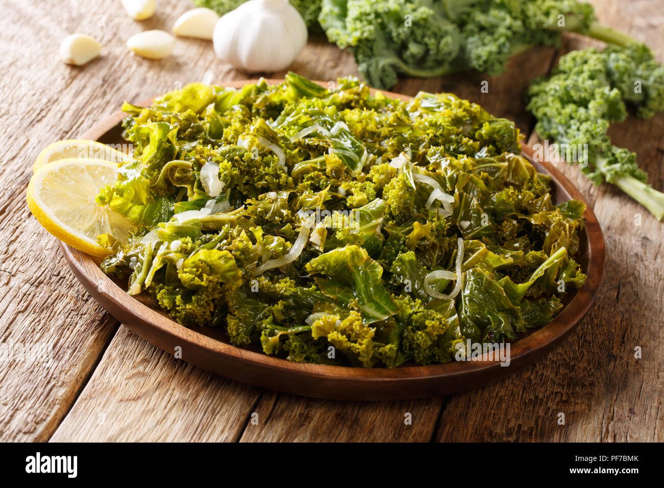Cavolo verde o una foglia di cavolo cotto con cipolle, aglio, olio di oliva e limone close-up su una piastra su un piano orizzontale. Foto Stock