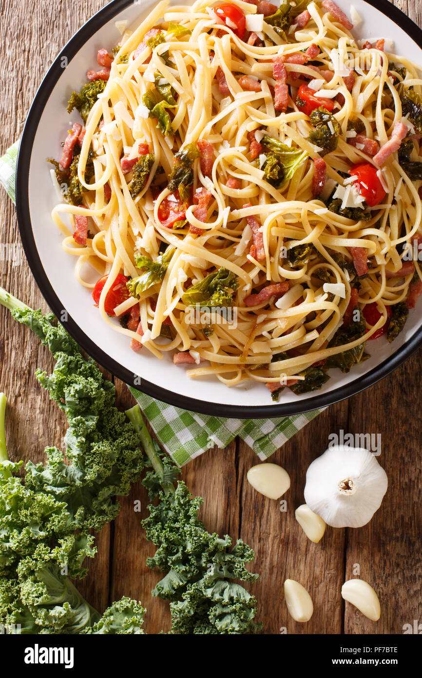 Pasta Linguine con cavolo rapa, pancetta, pomodori e parmigiano close-up su una piastra. Verticale in alto vista da sopra Foto Stock