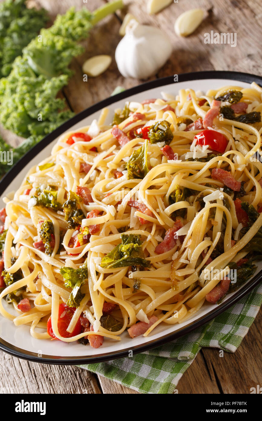 Pasta Linguine con cavolo rapa, pancetta, pomodori e parmigiano close-up su una piastra verticale. Foto Stock