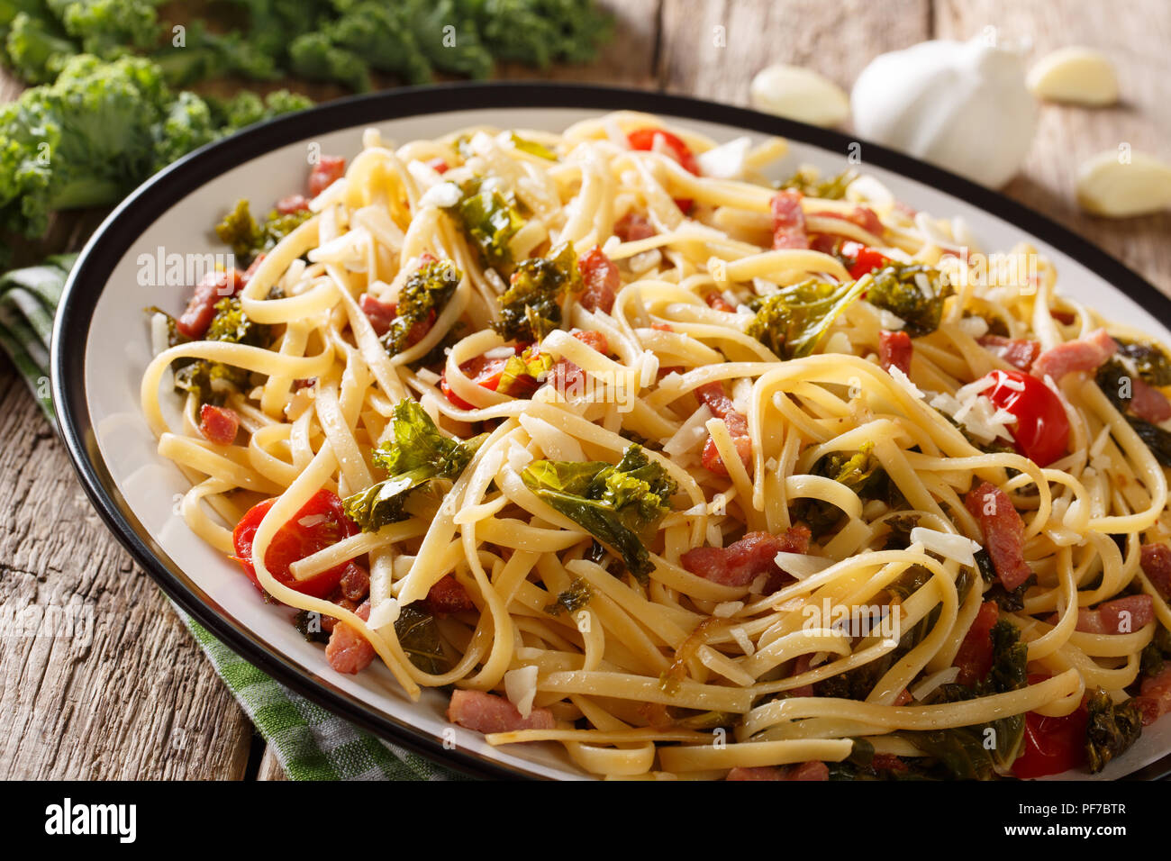 Pasta fatta in casa con kale fritte, pancetta, pomodori, aglio e parmigiano close-up su una piastra orizzontale. Foto Stock