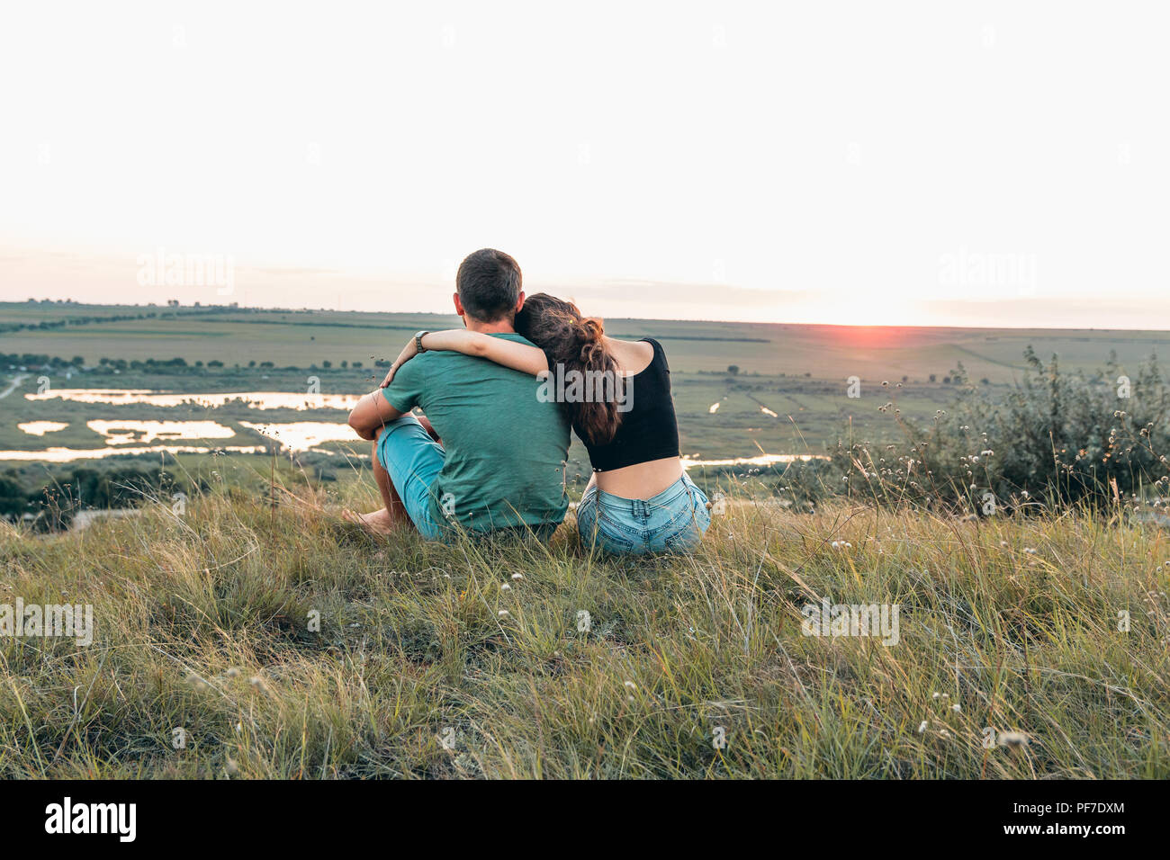Giovane è avvolgente e seduta vicino su una collina al tramonto Foto Stock