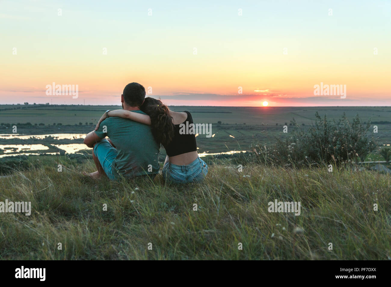 Giovane è avvolgente e seduta vicino su una collina al tramonto Foto Stock