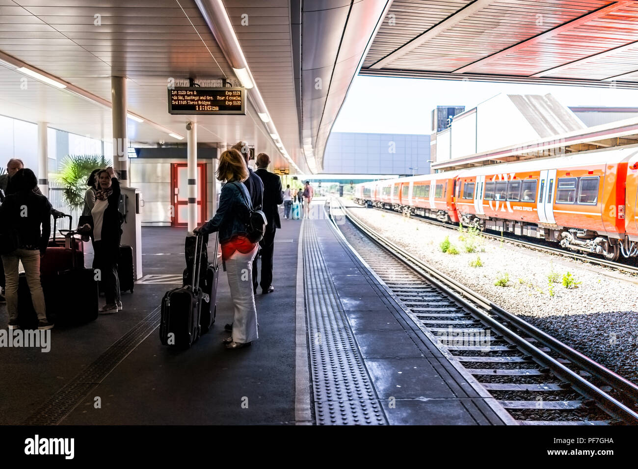 Horley, Regno Unito - 28 Giugno 2018: Gatwick Express metro e con il rosso arancio treno della metropolitana di Londra aeroporto, persone in attesa sulla stazione della piattaforma Foto Stock