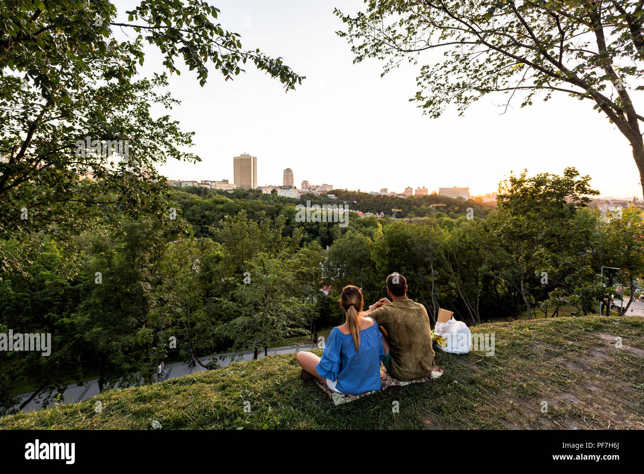 Kiev, Ucraina - 10 agosto 2018: il paesaggio vicolo in Kiev città capitale durante il tramonto dorato con luce solare giovane seduto sul picco di collina guardando citysc Foto Stock