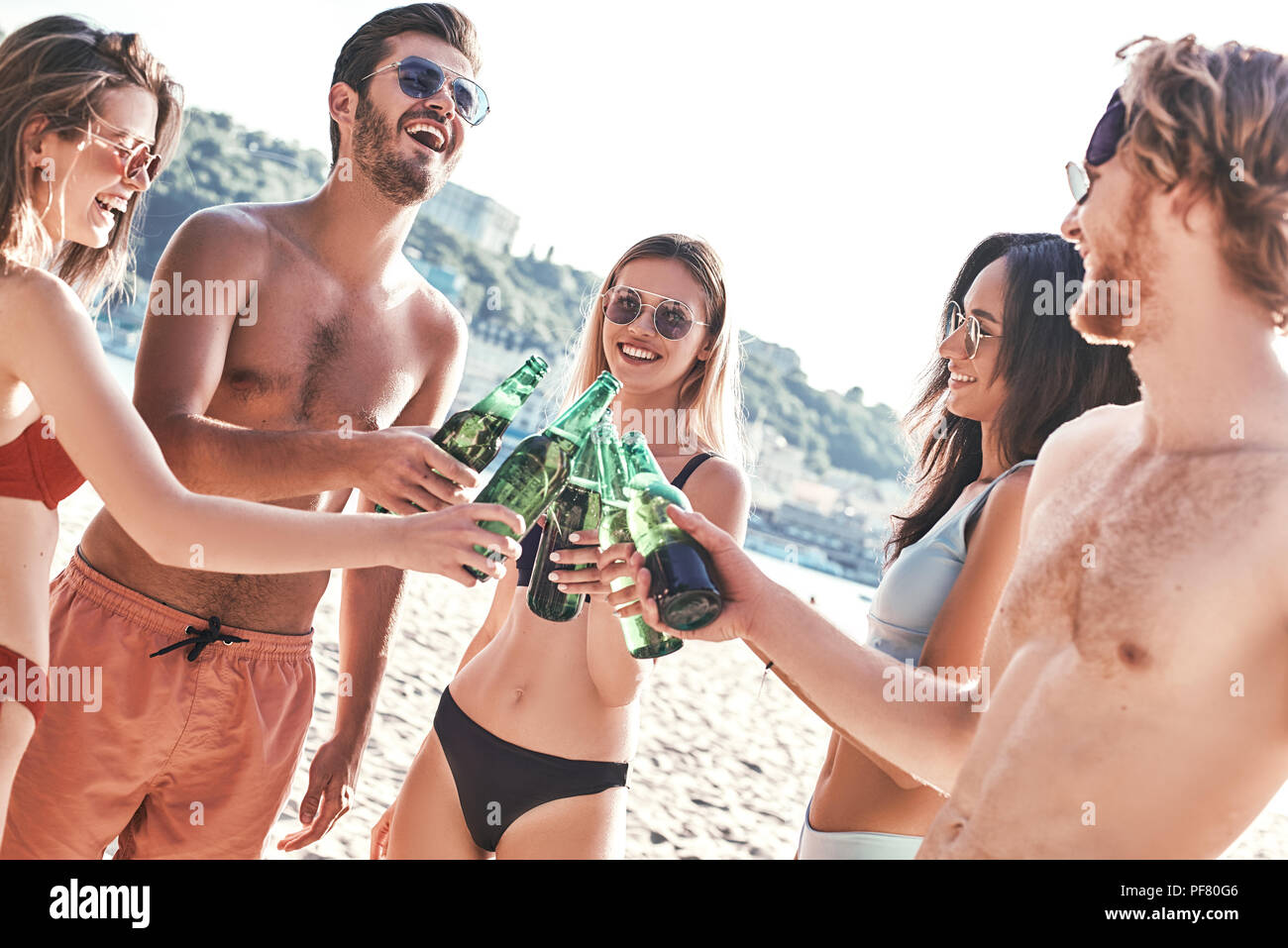 Godendo di spensierata il tempo con gli amici. I giovani allegri trascorrere del tempo piacevole insieme mentre è seduto sulla spiaggia e bere birra Foto Stock