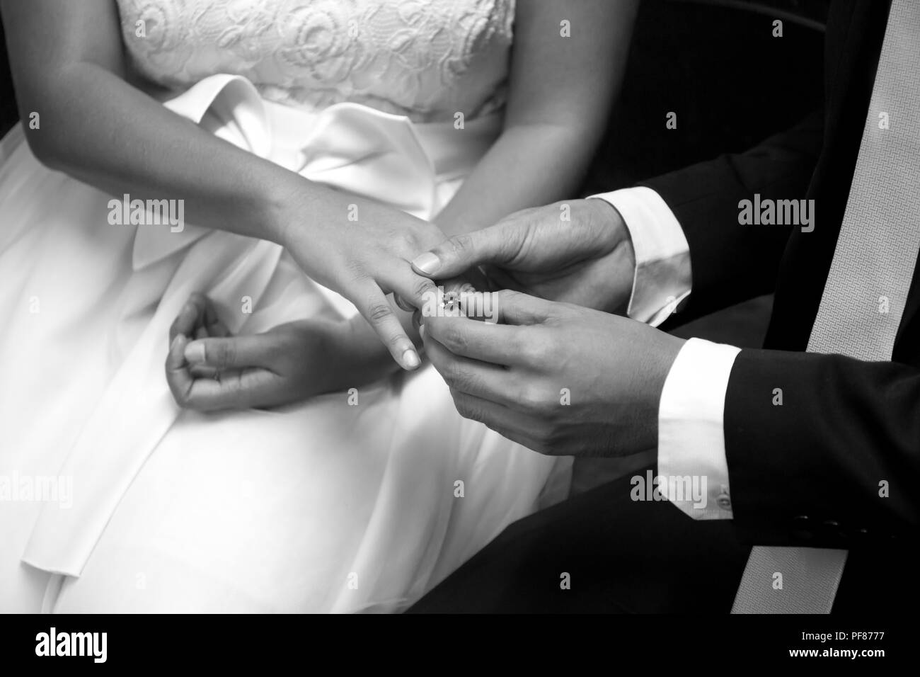 Lo sposo di mettere un anello di nozze su sposa il dito in bianco e nero Foto Stock