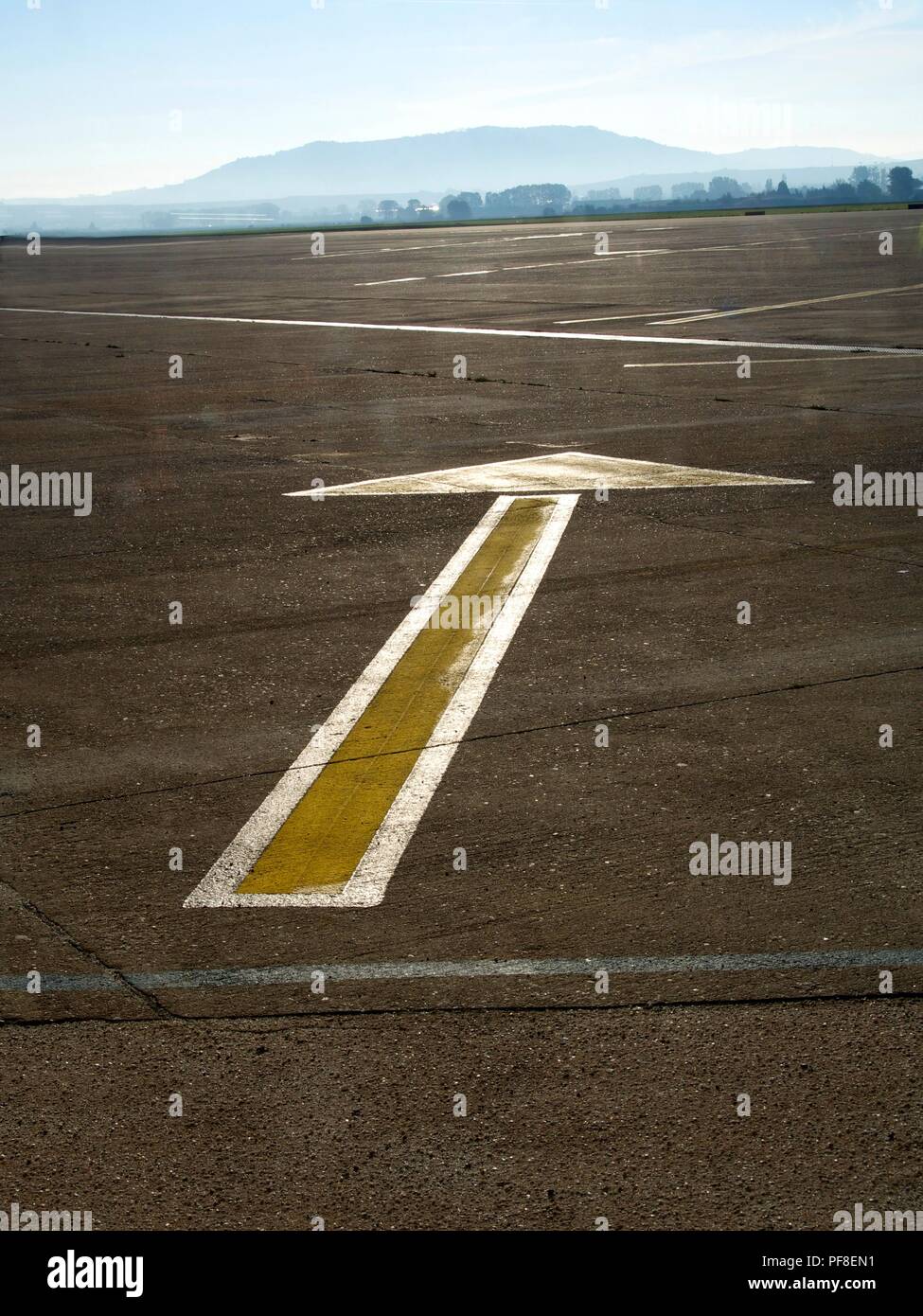 Scatto verticale ad angolo alto di una freccia dipinta di giallo a terra che punta dritto in avanti. Asfalto di un aeroporto. Foto Stock