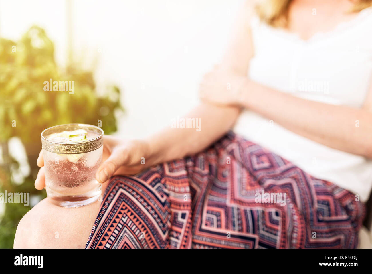 Donna bionda rilassante sul patio holding bevanda ghiacciata Foto Stock