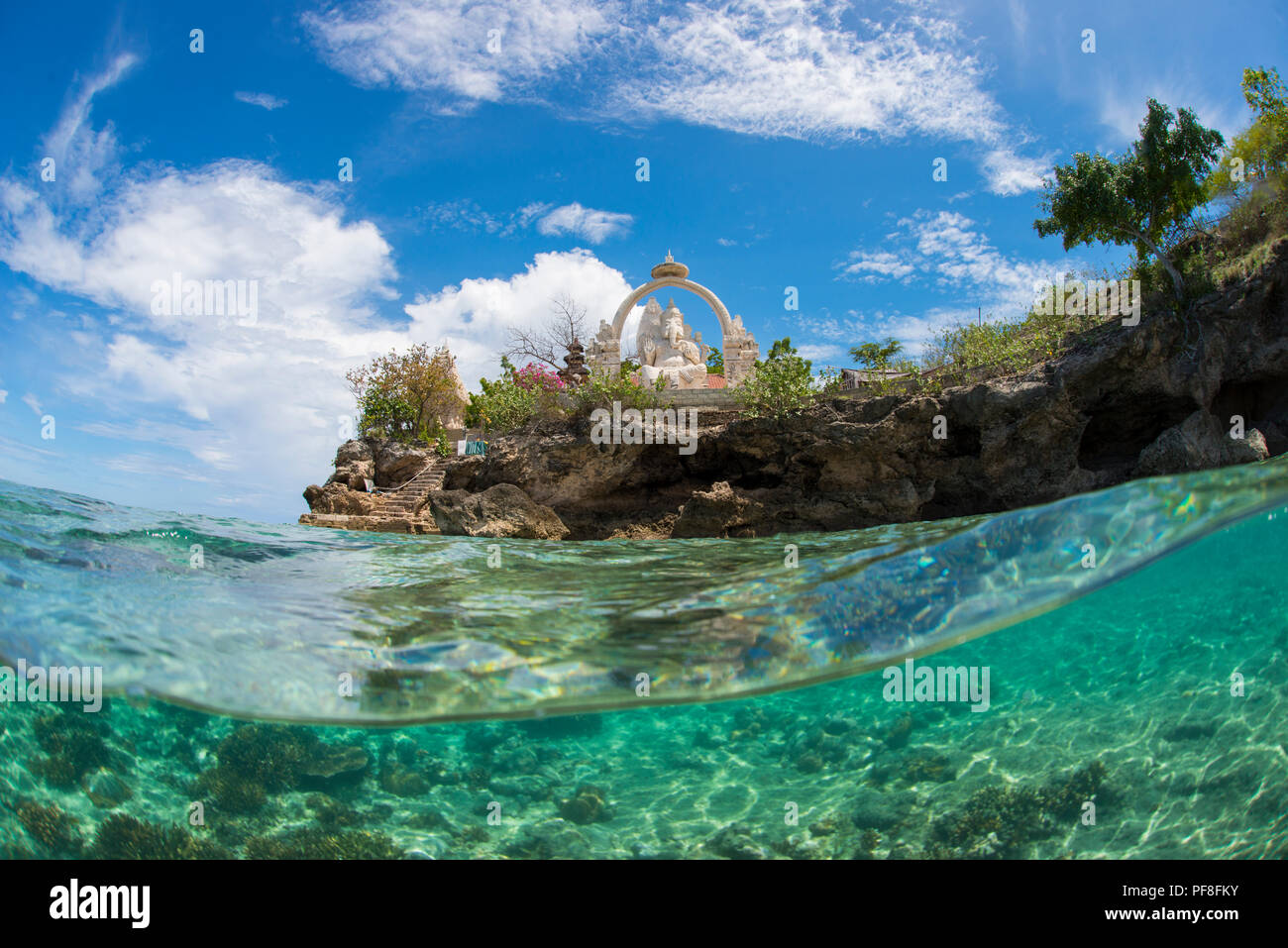 Underwater split-livello foto in poco profonde acque tropicali del tempio buddista & Ganesh statua all'Isola Menjangan, Bali, Indonesia, con il blu del cielo sopra. Foto Stock