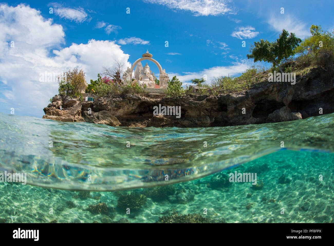 Underwater split-livello foto in poco profonde acque tropicali del tempio buddista & Ganesh statua all'Isola Menjangan, Bali, Indonesia, con il blu del cielo sopra. Foto Stock