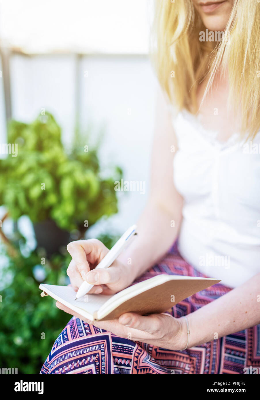 Donna seduta sul patio prendendo appunti per i notebook Foto Stock