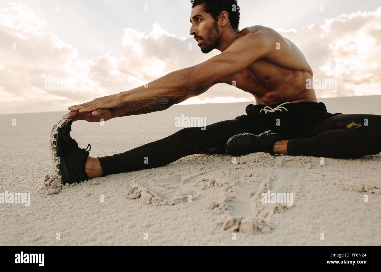 Atleta facendo stretching seduta di allenamento sulla duna di sabbia. Runner seduto nel deserto e lo stiramento delle gambe. Foto Stock