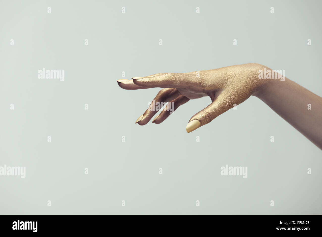 Una mano di donna in vernice oro su sfondo grigio. Mano di donna dipinta con colori dorati. Foto Stock